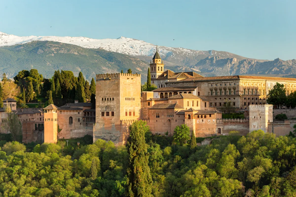The Alhambra in warm low light seen from the Mirador de San Nicolás, with the snow-topped Sierra Nevada behind it